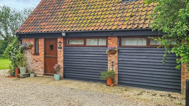 Une maison en briques avec un toit en tuiles, une porte d’entrée et deux portes de garage.