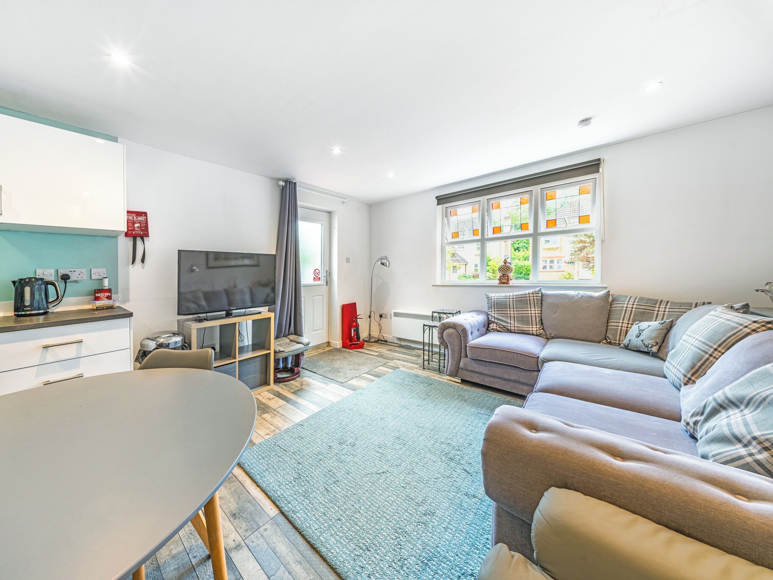 Una sala moderna con sofá, televisión, mesa de comedor y cocina equipada con hervidor y tostadora.