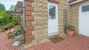 A stone house with a white door, a small porch with potted plants, and a brick pathway.