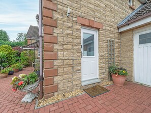 A stone house with a white door, a small porch with potted plants, and a brick pathway.