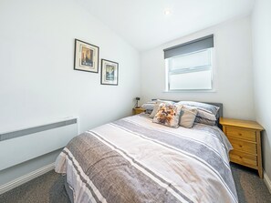 A bedroom with a bed, a nightstand, a window with blinds, and two framed pictures on the wall.