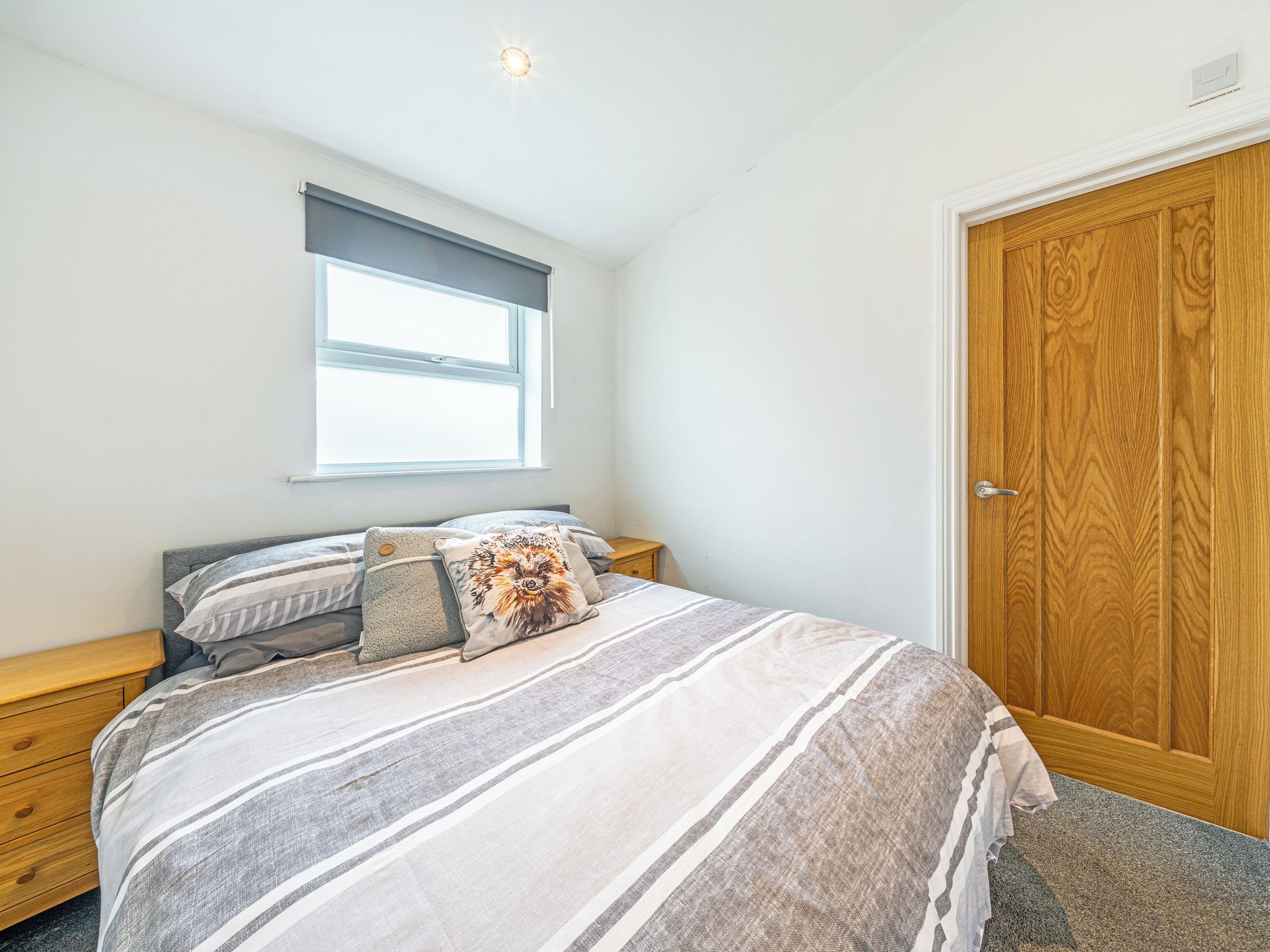 A bedroom with a bed, a window, a wooden door, and a nightstand.