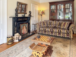 Un salon avec une cheminée, un canapé, une bibliothèque et une table d’échecs.