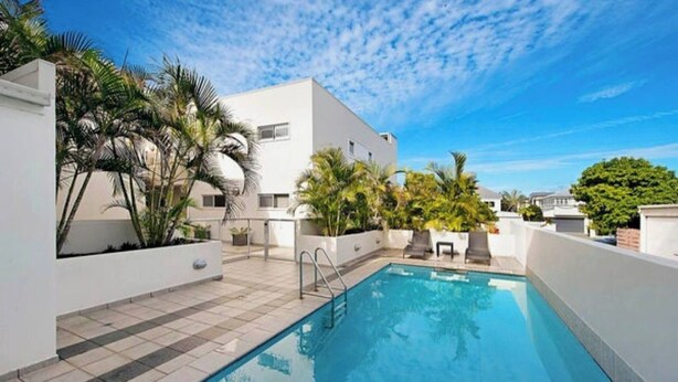 A swimming pool with a tiled deck, surrounded by white walls and palm trees.