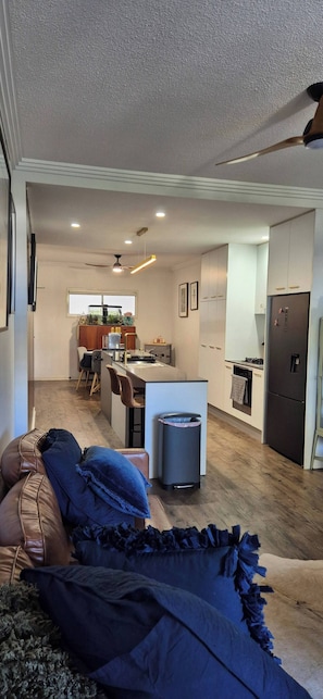 A modern living room with a sofa, a dining area with chairs, a kitchen with a refrigerator, and a ceiling fan. - A perfect place to hide away with river side charm (Balmoral)
