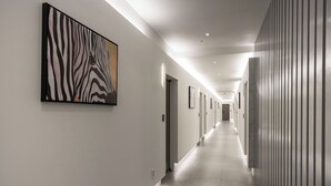Un lungo corridoio ben illuminato con un'opera d'arte a motivi zebrati sulla parete sinistra, porte lungo la destra e un pavimento piastrellato.