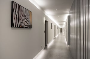 A long, well-lit hallway with a zebra print artwork on the left wall, doors along the right, and a tiled floor.