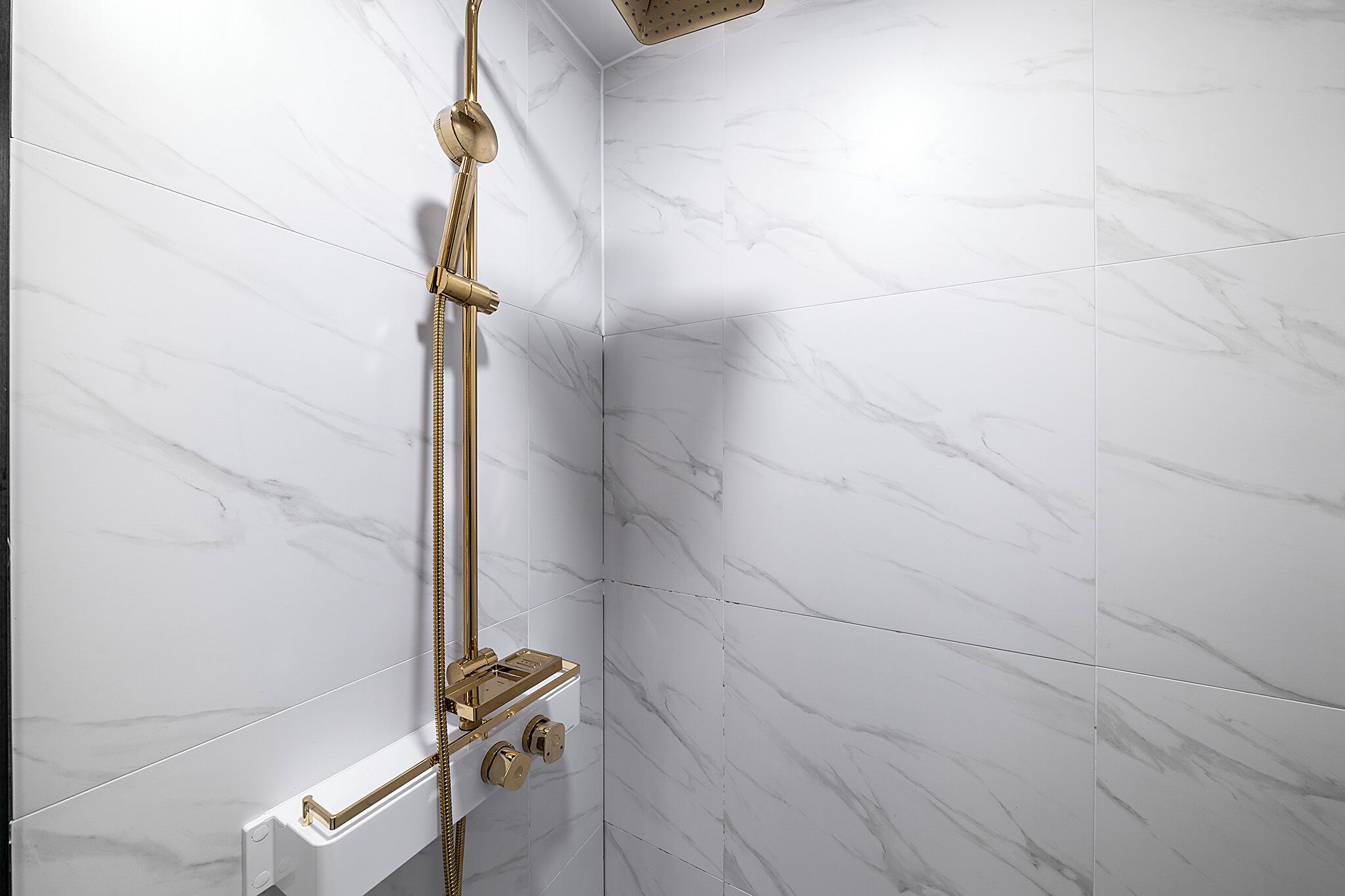 Une douche dotée d’une robinetterie dorée, dans une salle de bain carrelée de marbre blanc.