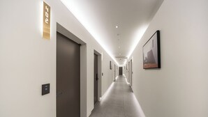 Un lungo e stretto corridoio con porte su entrambi i lati, un lampadario a soffitto e un quadro appeso alla parete destra.