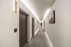Un pasillo largo y estrecho con puertas a ambos lados, una lámpara en el techo y un cuadro en la pared derecha.