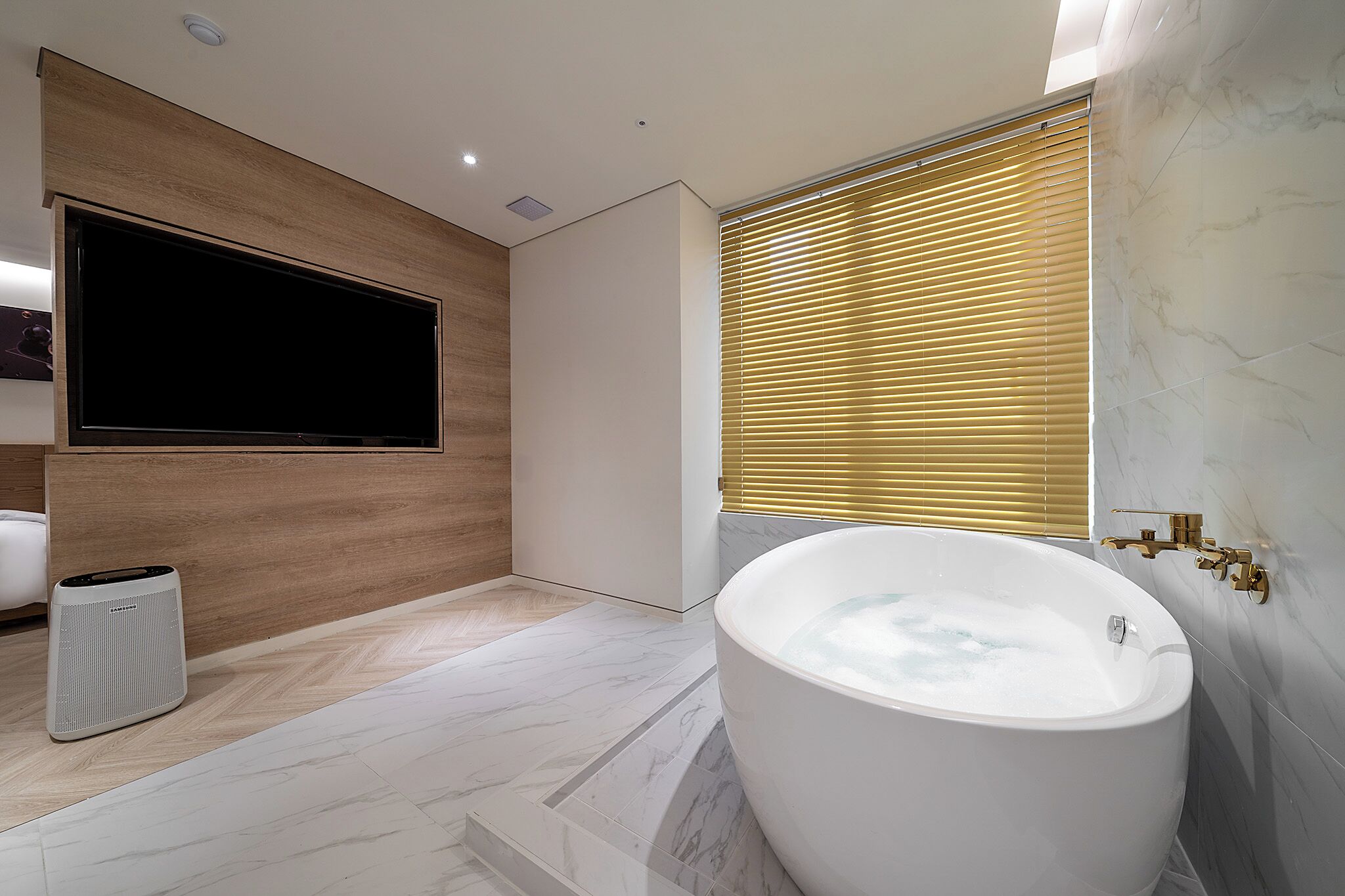 A modern bathroom with a freestanding bathtub, a wall-mounted TV, and a trash can.