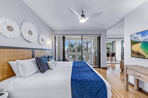 Een moderne hotelkamer met een groot bed, een plafondventilator en een balkon met uitzicht op het strand.