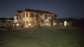 Casa de dos pisos con patio cercado, un pequeño jardín e iluminación en la entrada.