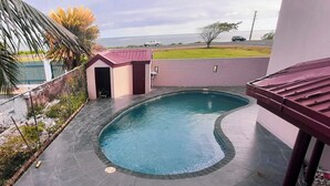 Een zwembad met een gebogen rand, een klein gebouw met een rood dak en uitzicht op de oceaan.