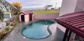 Una piscina de borde curvo, una pequeña estructura con techo rojo y vista al océano.