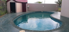 A swimming pool with a curved edge, surrounded by a tiled deck.