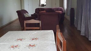 Een ruime woonkamer met een zithoek, een eettafel met bloemenonderzetter en een kledingkast.