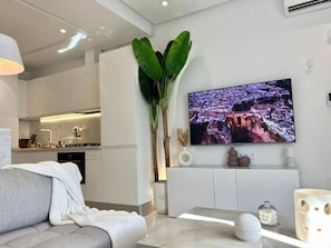 A modern living room with a flat-screen TV, a large plant, and a sofa. - Hirondelle de Sidi Bou Saïd-Appartement Terrasse (Sidi bou said)