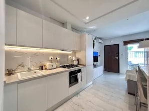 A modern kitchen with white cabinets, a marble countertop, a built-in oven, and a small island with a sink. - Hirondelle de Sidi Bou Saïd-Appartement Terrasse (Sidi bou said)