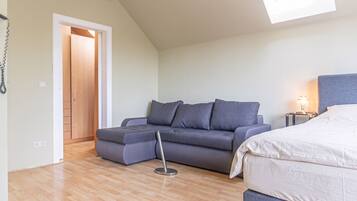 A room with a sofa, a bed, a standing lamp, and a door leading to another room.