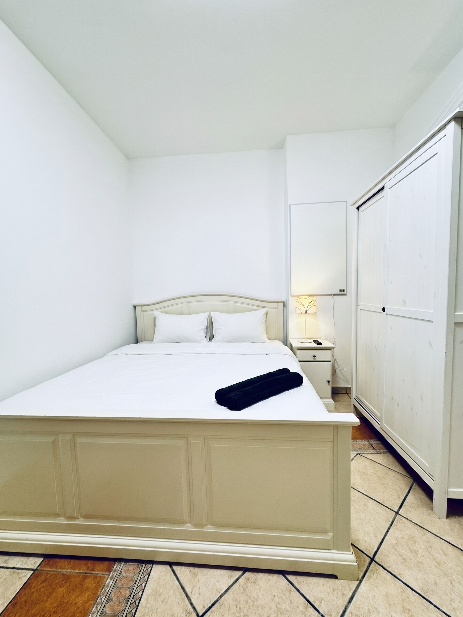 A bedroom with a bed, a nightstand, a lamp, and a wardrobe.