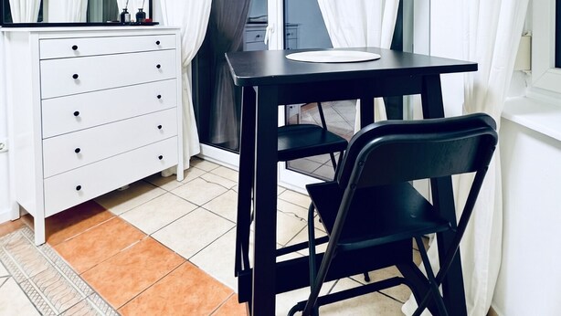 A room with a white dresser, a round mirror, a black desk, a black chair, and white curtains. - Cozy Room With Shared Garden Access (Vienna)