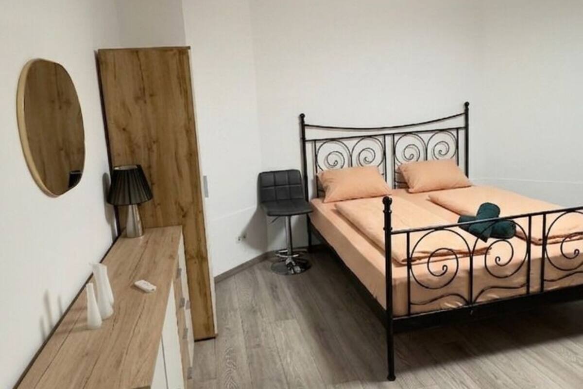 A bedroom with a bed, a wooden desk, a mirror, a lamp, and a wardrobe.
