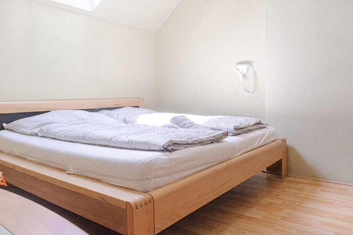 A single bed in a room with a sloped ceiling and a wall-mounted phone.