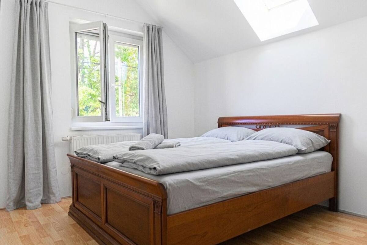 A bedroom with a wooden bed, a window with curtains, and a skylight.