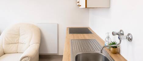 A modern kitchen with a stainless steel sink, wooden countertop, and a white chair.