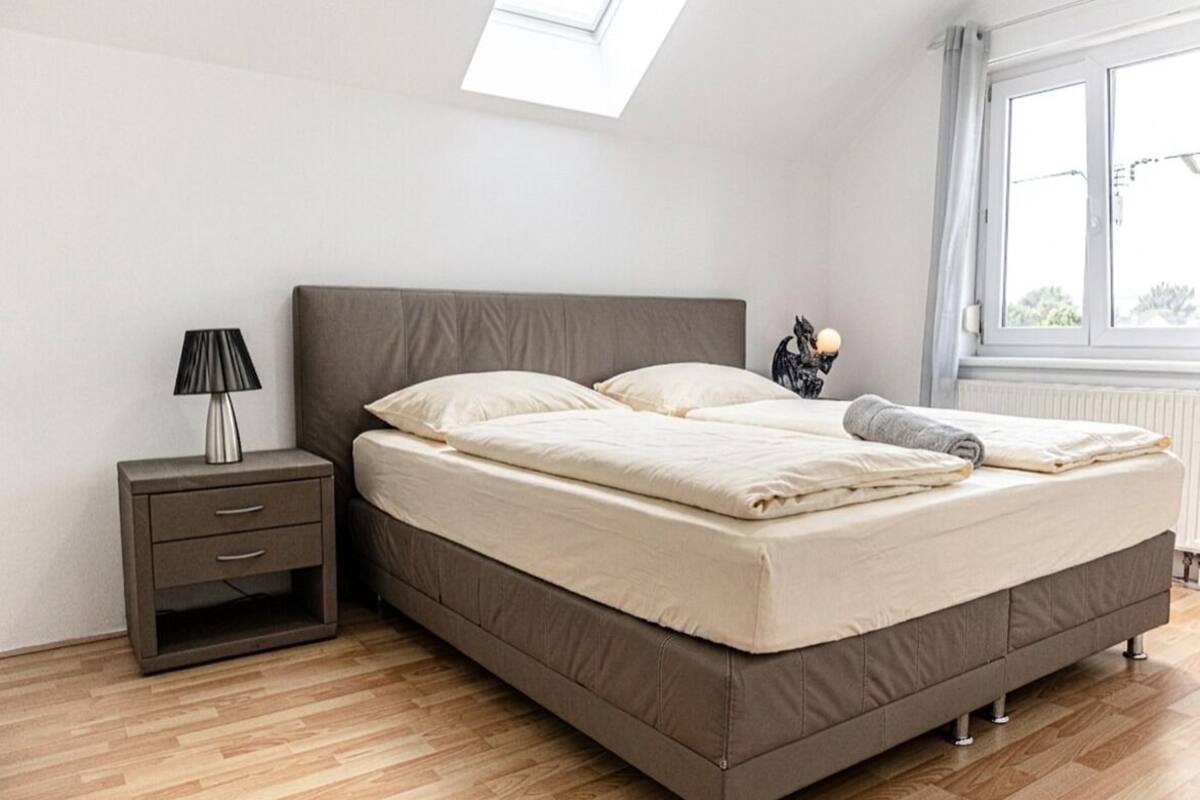 A bedroom with a bed, a nightstand, a lamp, and a window.