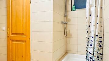A bathroom with a wooden door, a shower with a curtain, and a small shelf with toiletries.