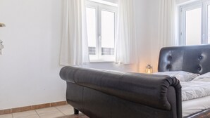 A bedroom with a dark-colored bed, white curtains, a window, and a small table with a lantern. - Cozy Room With Shared Garden Access (Vienna)