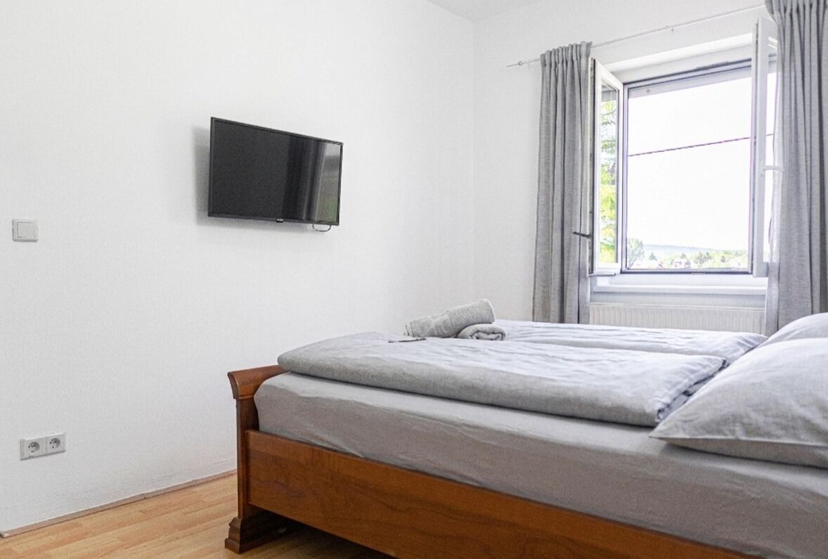 Un dormitorio con cama, televisión montada en la pared y ventana con cortinas.