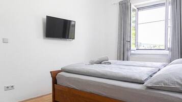 Un dormitorio con cama, televisión montada en la pared y ventana con cortinas.