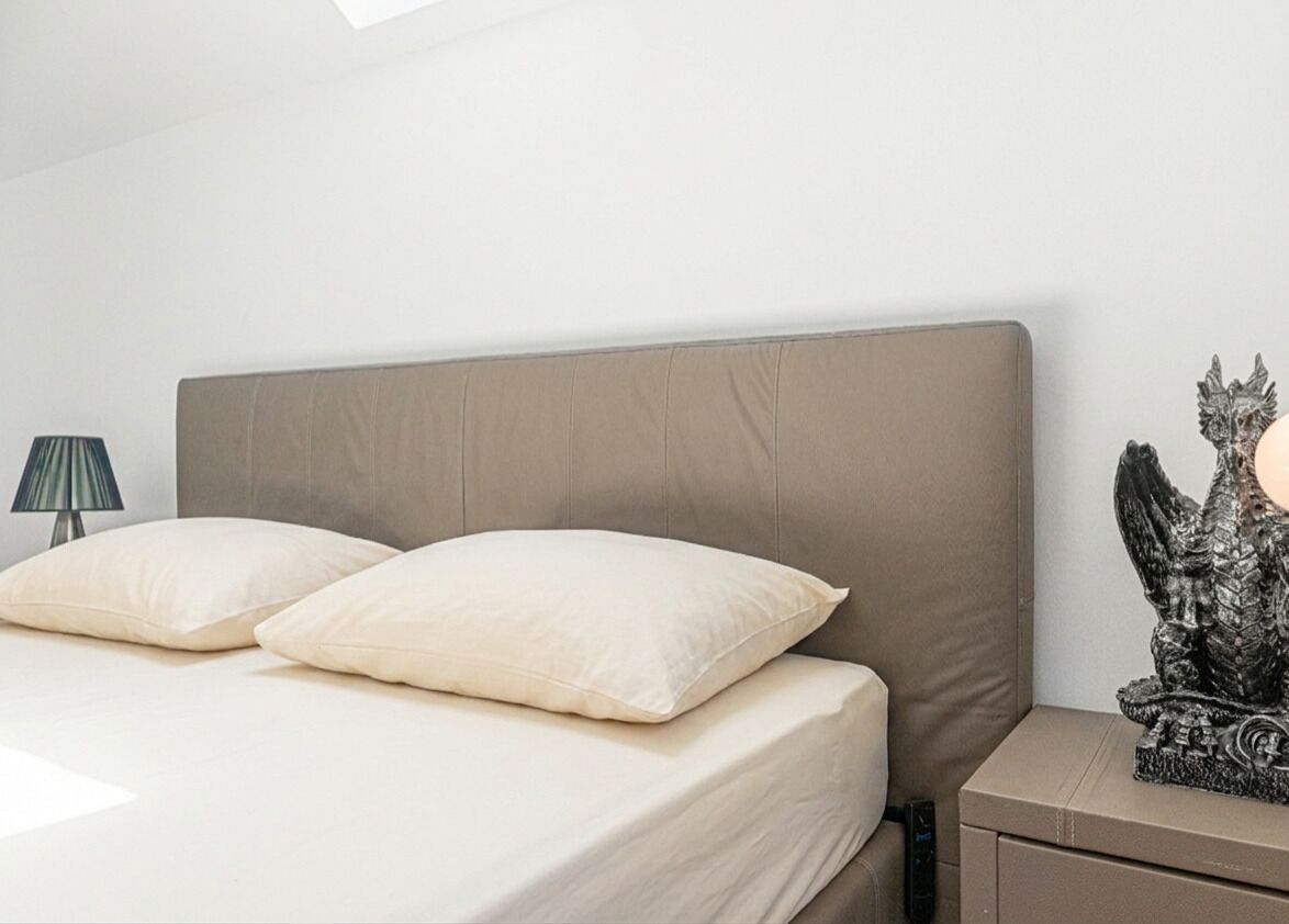 Een bed met hoofdbord, twee kussens, nachtkastje met lamp en decoratief beeld.