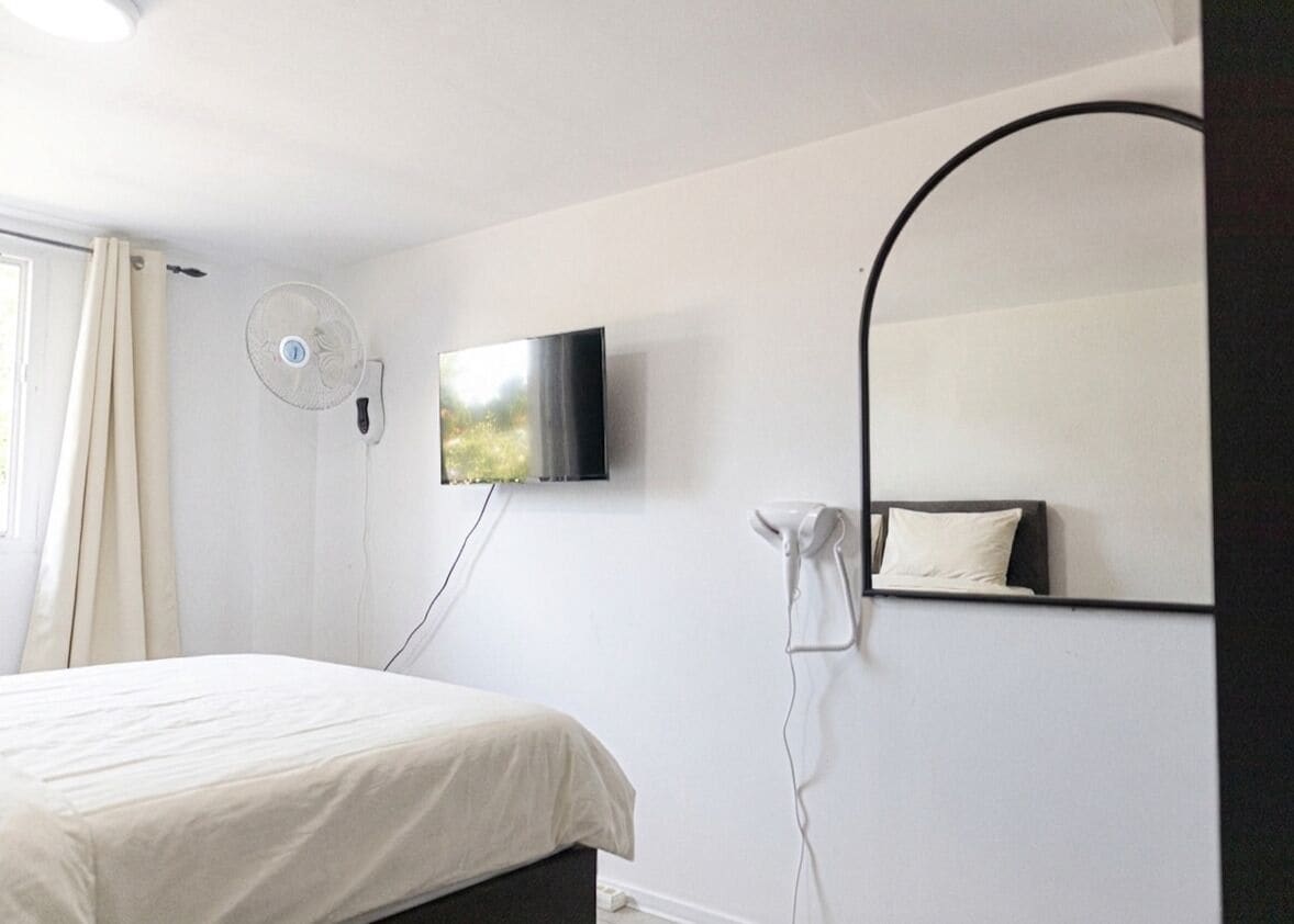 Un dormitorio con cama, televisor de pared, ventilador, secador de pelo y espejo.