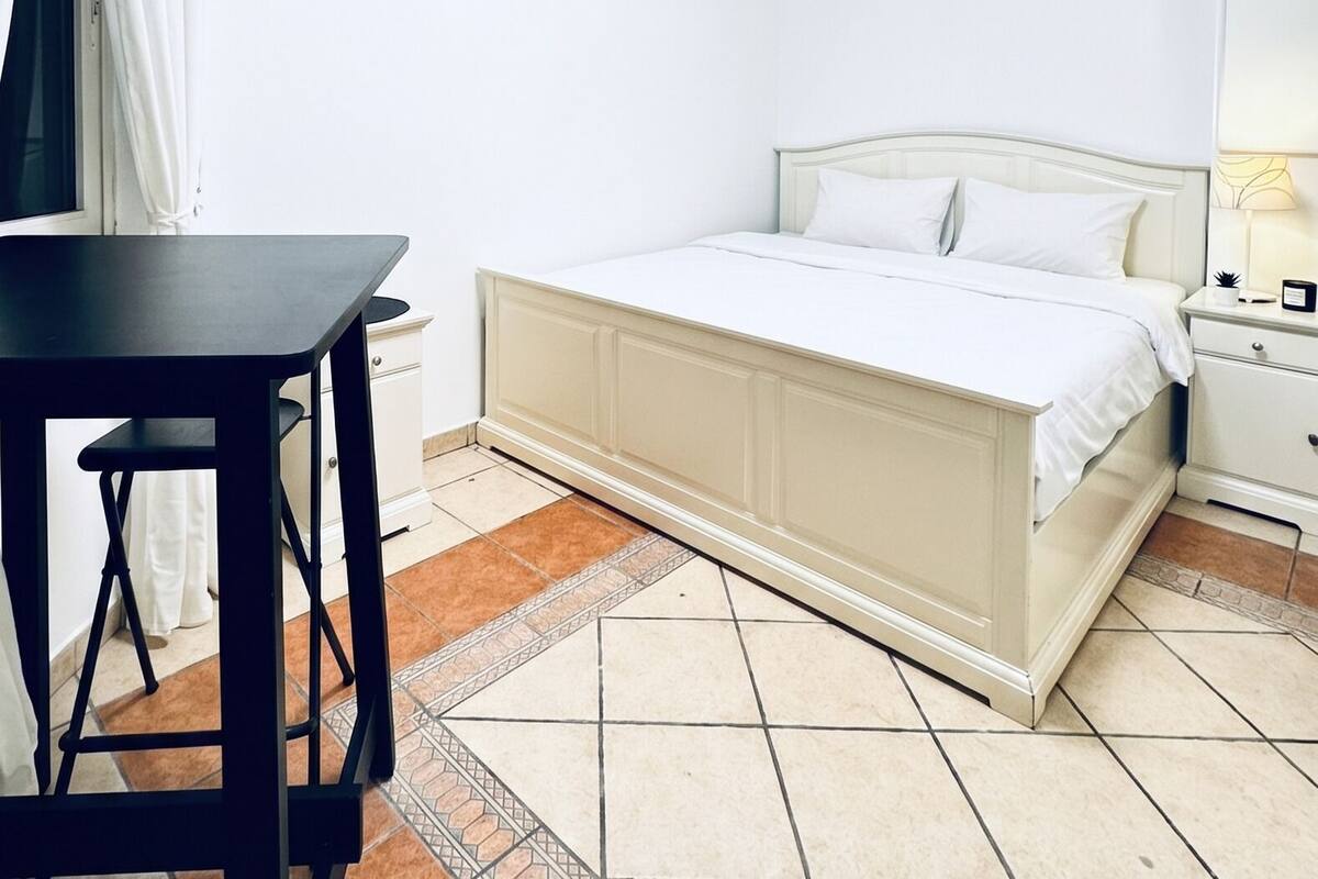 A bedroom with a bed, a bedside table, a lamp, and a window with curtains.