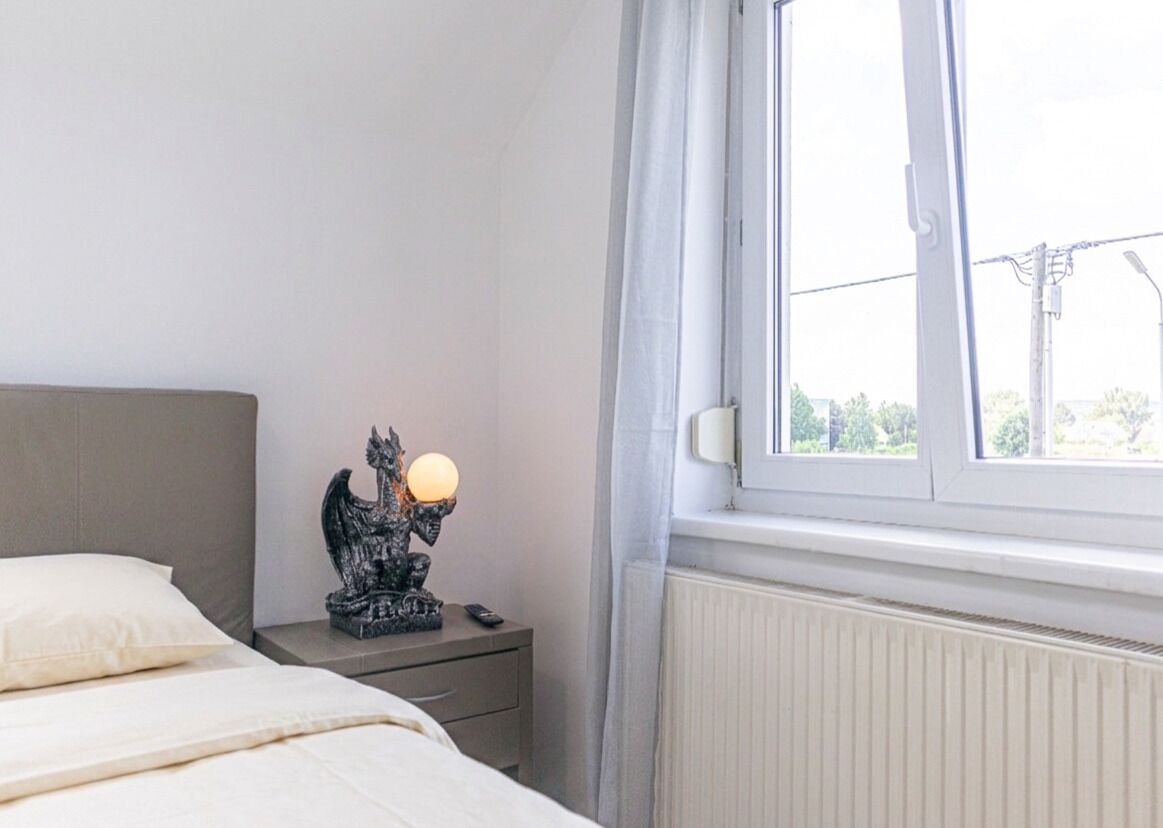 Een slaapkamer met een bed, een nachtkastje met lamp en een raam met uitzicht.