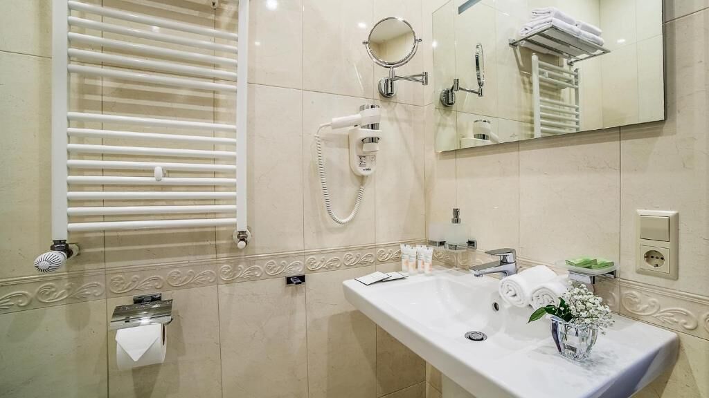 A modern bathroom with a large mirror, a towel rack, a hairdryer, and a sink with toiletries.