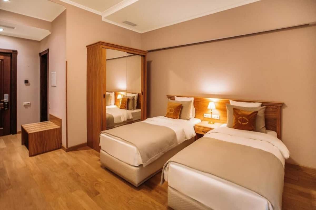 A hotel room with two beds, a wooden wardrobe, a small wooden stool, and a mirror.