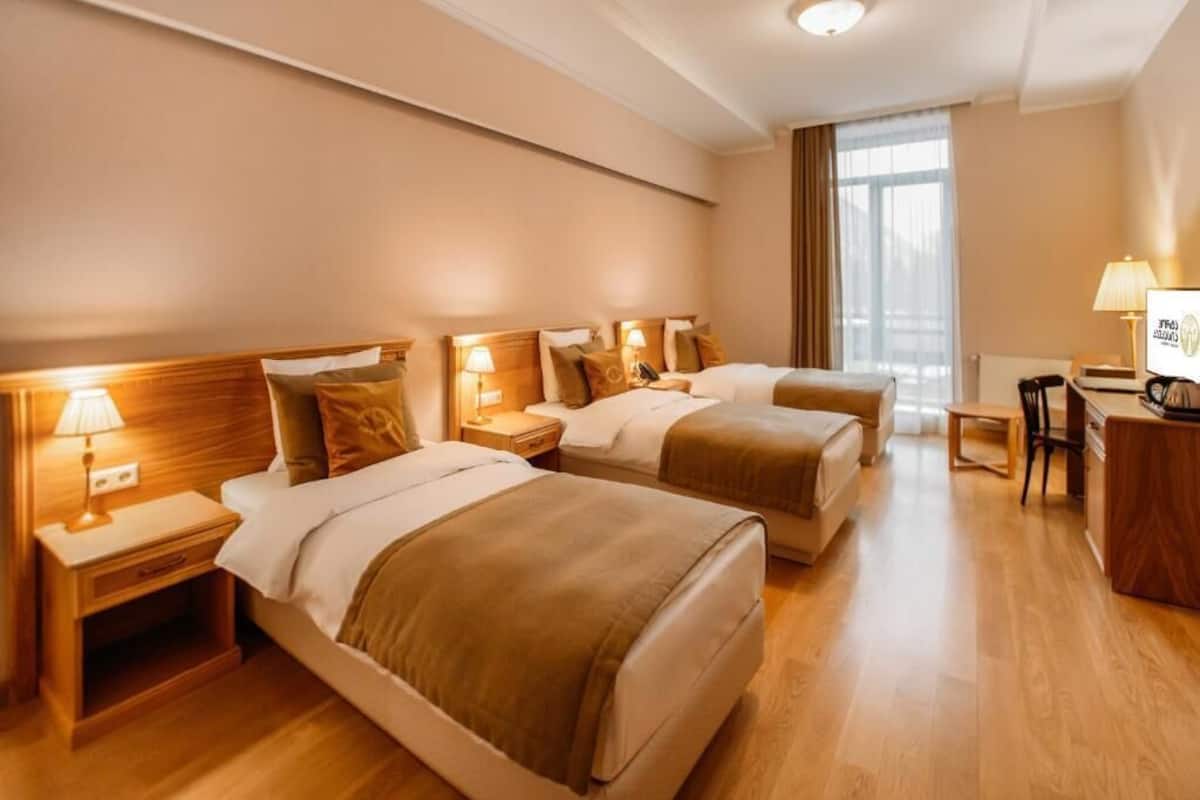 A hotel room with two beds, wooden headboards, bedside tables with lamps, a desk, and a chair.