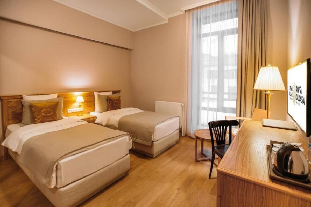 A hotel room with two beds, a desk, a chair, a lamp, and a window with curtains.