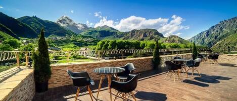 A terrace with outdoor seating, a mountain view, and a stone wall.