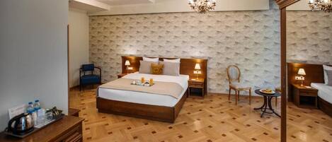 Quarto de hotel com cama grande, piso de madeira, lustre e espelho.