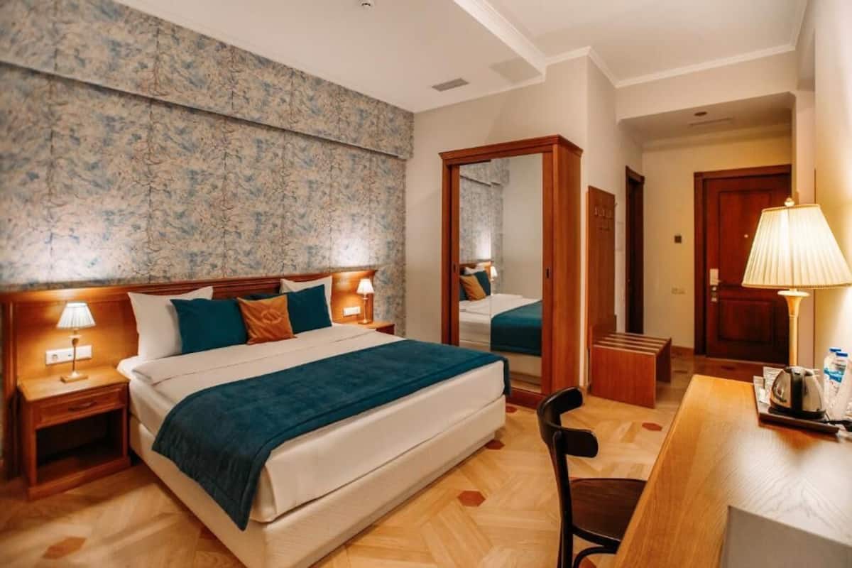 A hotel room with a bed, bedside tables, a desk, a chair, a mirror, and a door.