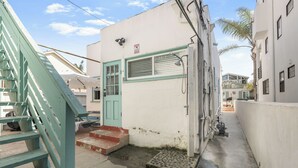 Une ruelle étroite avec un bâtiment blanc, doté d’une porte verte et d’un escalier menant à une petite entrée.