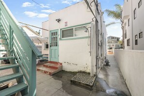 A narrow alleyway with a white building featuring a green door and steps leading to a small entrance. - Walk to Beach + Breezy Coastal 1BR | Shared Patio + Dining | Ormond Court Unit 3 (San Diego)