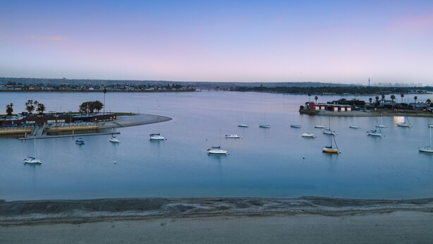 Un port de plaisance où sont amarrés de nombreux bateaux, une plage de sable et, au loin, le profil d’une ville.