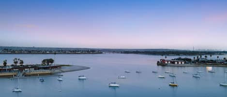 A marina with multiple boats docked, a sandy beach, and a distant city skyline.